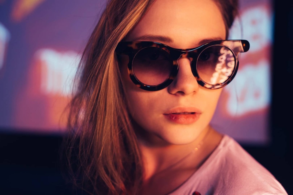 Kobieta nosząca okulary przeciwsłoneczne znajduje się przed ekranem, emanując elegancją i nowoczesnością.