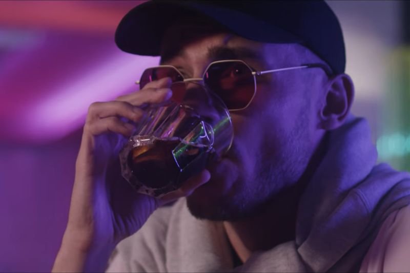 Pezet w kapeluszu i czapeczce delektuje się drinkiem w teledysku Magenta.