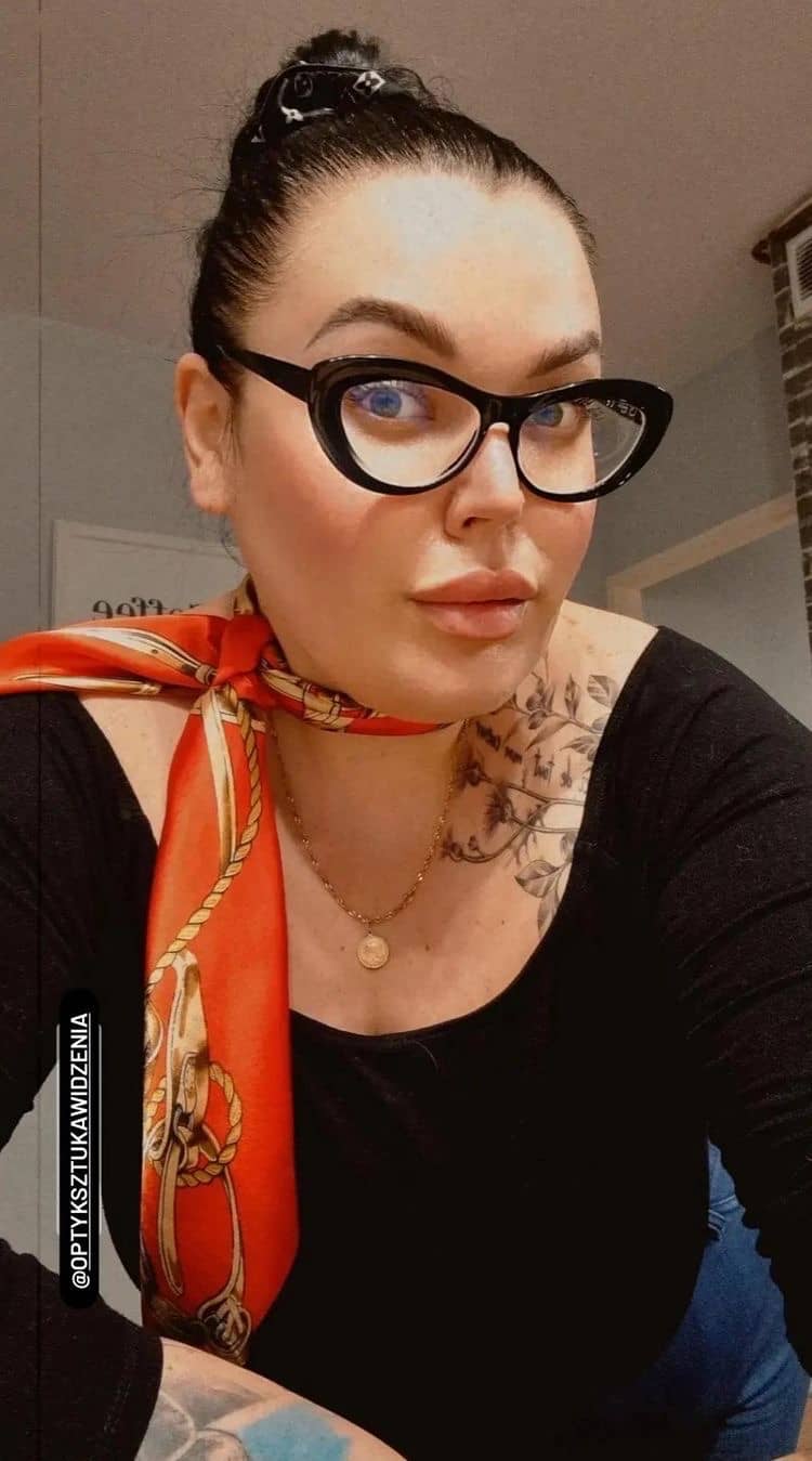 Klientka w okularach z tatuażami, ubrana w czerwoną chustę, emanująca indywidualnością i pewnością siebie.