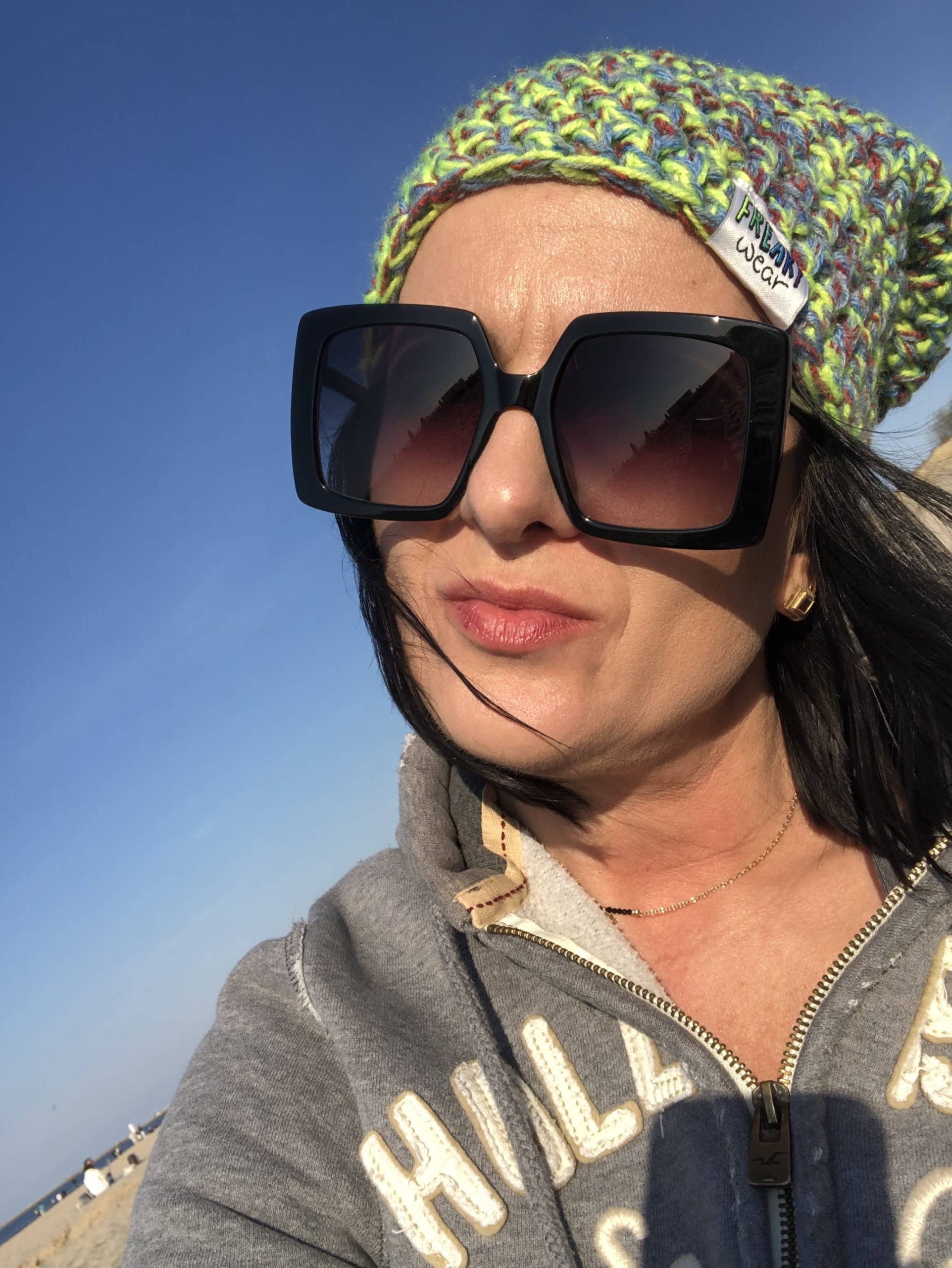Właścicielka salonu w modnych okularach przeciwsłonecznych, odpoczywająca na plaży, otoczona piaskiem i morzem.